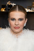 Woman with styled hair and makeup, wearing a white feathered garment, with decorative background.